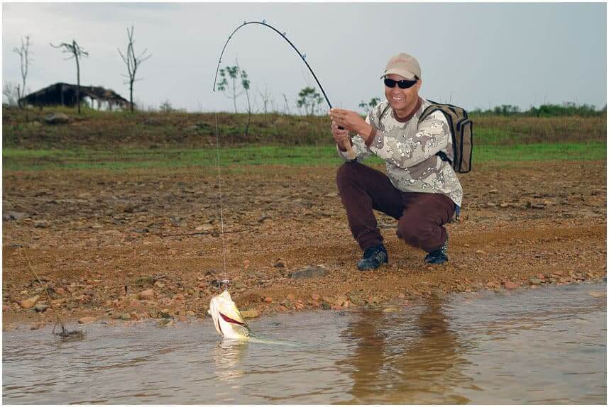 pescador capturando um peixe com vara de pesca no pesqueiro